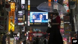 Pejalan kaki berjalan melewati TV publik raksasa dengan siaran langsung konferensi pers oleh PM Jepang Yoshihide Suga yang mengumumkan keadaan darurat akibat meningkatnya kasus virus corona di Tokyo, Kamis, 8 Juli 2021. (AP Photo/Eugene Hoshiko)
