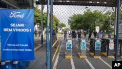 Brazilian Ford workers stand at the entrance to the partially closed plant as they listen to union leaders in Taubate, Brazil, Jan. 12, 2021, the day after Ford Motor Co. announced it will close three plants in Brazil.