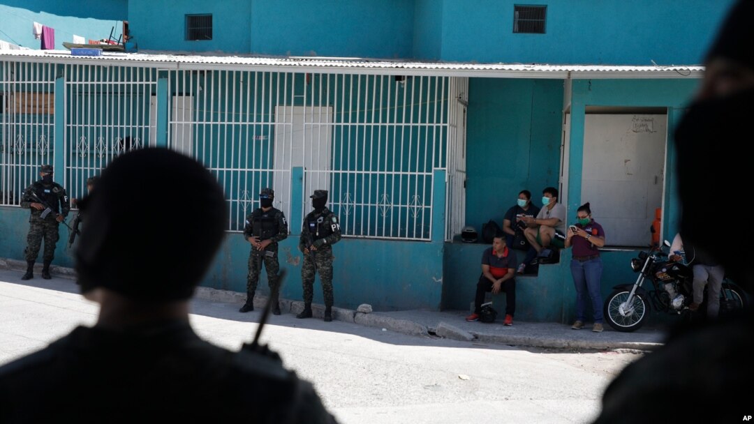 Hondureños usando mascarillas observan cómo soldados y policías acordonan un barrio en el que se detectaron varios casos de coronavirus, durante los días más severos del confinamiento que ya comienza a relajarse.