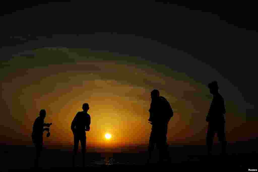 Palestinians stand on a beach during sunset in Gaza City.