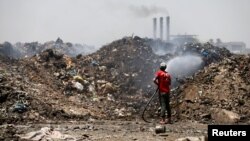 A municipal worker extinguishes a fire inside the garbage at a rubbish dump in Baghdad, Iraq, May 30, 2019. 