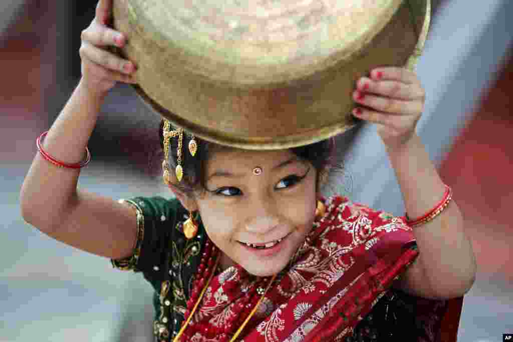 A young girl wearing traditional attire plays with a vessel while waiting for the Kumari puja to start at Hanuman Dhoka temple, in Kathmandu, Nepal.