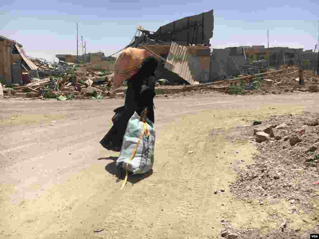 A woman drags a torn sack filled with personal belongings and carrying kitchen furniture on her left shoulder as she flees Islamic State rockets in al-Zanjili neighborhood in Mosul, Iraq, May 31, 2017. (K.Omar/VOA)