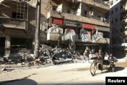 FILE - People ride a cart pulled by a horse near the damaged al-Hakeem hospital, in the rebel-held besieged area of Aleppo, Syria, Nov. 19, 2016.