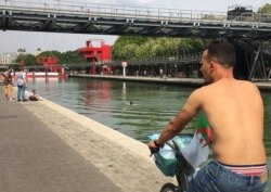 A man rides his bike shirtless as another takes a dip in La Villette basin, in Paris, France. (L. Bryant/VOA)