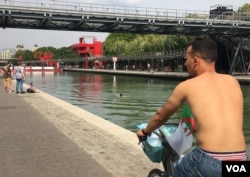 A man rides his bike shirtless as another takes a dip in La Villette basin, in Paris, France. (L. Bryant/VOA)