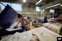 I lavoratori stirano i vestiti presso lo stabilimento Cose di Maglia dove viene prodotto il marchio outdoor D., a Brescia, in Italia, il 14 giugno 2022 (AP Photo/Luca Bruno)