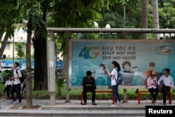 FILE - Internet users browse internet near an advertising billboard for 4G connection service at a bus-stop in Hanoi, Vietnam.