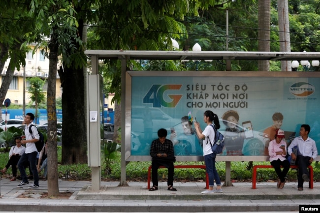 FILE - Internet users browse internet near an advertising billboard for 4G connection service at a bus-stop in Hanoi, Vietnam.