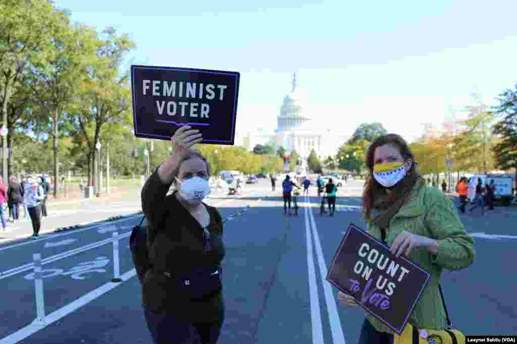 Duas mulheres fotografadas com o capit&#243;lio ao fundo exibem cartazes a dizer &quot;Eleitora Feminista&quot; e &quot;Conta conosco para votar&quot;. Marcha das Mulheres, 17 de outubro 2020