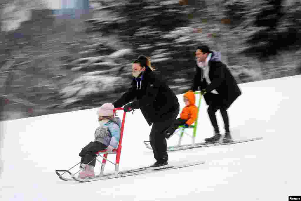 Laura Schulman and her daughter Cleo (L) ride a standing sled as her husband Nev and son Bo Schulman follow behind at Cedar Hill in Central Park in Manhattan after a winter storm in New York City, Feb. 2, 2021.