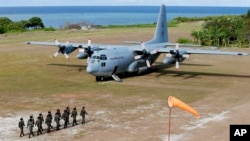 FILE - Philippine troops march as a Philippine Air Force C-130 transport plane carrying Philippine Defense Secretary Delfin Lorenzana, Armed Forces Chief Gen. Eduardo Ano and other officials, sits on the tarmac at the Philippine-claimed Thitu Island.