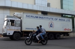 Men ride on a motorbike past a supply truck of India's Serum Institute, the world's largest maker of vaccines, which is working on a vaccine against the coronavirus disease (COVID-19) in Pune, India, May 18, 2020