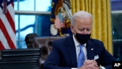 President Joe Biden pauses as he signs his first executive orders in the Oval Office of the White House on Jan. 20, 2021, in Washington.