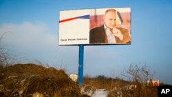 FILE - A partially damaged billboard with a portrait of Russian President Vladimir Putin is seen on a roadside near Simferopol, in Russia-annexed Crimea, Jan. 24, 2016. The billboard reads: "Crimea. Russia. Forever."