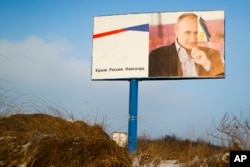 FILE - A partially damaged billboard with a portrait of Russian President Vladimir Putin is seen on a roadside near Simferopol, Crimea, Jan. 24, 2016. The billboard reads: "Crimea. Russia. Forever."