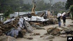 Residents walk by overturned cars as they leave with their belongings after a landslide in Teresopolis, Brazil, 13 Jan 2011