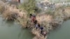 Un grupo de migrantes intenta atravesar una valla de alambre a orillas del río Grande mientras miembros de la Guardia Nacional de EEUU hacen guardia al otro lado de la valla en Eagle Pass, Texas, Estados Unidos, el 27 de febrero de 2024.