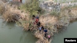 Un grupo de migrantes intenta atravesar una valla de alambre a orillas del río Grande mientras miembros de la Guardia Nacional de EEUU hacen guardia al otro lado de la valla en Eagle Pass, Texas, Estados Unidos, el 27 de febrero de 2024.