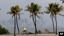 FILE - The Miami skyline is shrouded in clouds as a cyclist rides along Biscayne Bay at Matheson Hammock Park, May 15, 2020, in Miami. A trough of low pressure was moving through the Florida Straits.