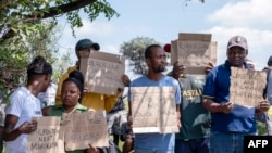 Membros da comunidade e trabalhadores seguram cartazes enquanto se juntam para protestar durante a operação de salvamento para retirar mineiros ilegais de uma mina de ouro abandonada em Stilfontein, a 14 de janeiro de 2025.