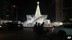 FILE - A man rides a motorcycle taxi past Christmas decorations on a street in Lagos, Nigeria, Dec. 20, 2024. 