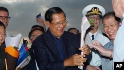File: Cambodia's Prime Minister Hun Sen, center, gives a flower to a passenger who disembarked from the MS Westerdam, owned by Holland America Line, at the port of Sihanoukville, Cambodia, Feb. 14, 2020.