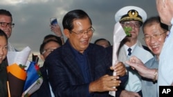 Cambodia's Prime Minister Hun Sen, center, gives a flower to a passenger who disembarked from the MS Westerdam, owned by Holland America Line, at the port of Sihanoukville, Cambodia, Feb. 14, 2020.