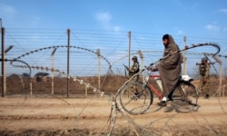 FILE - A man rides his bicycle past India's Border Security Force (BSF) soldiers patrolling the fenced border with Pakistan near Jammu, Jan. 28, 2010.