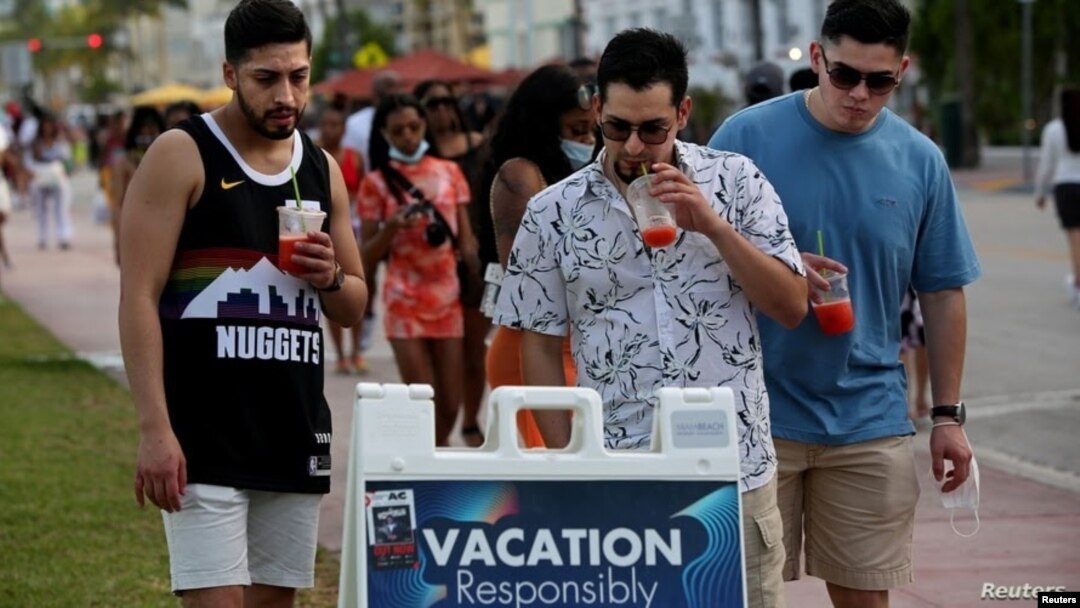 Hombres jóvenes leen las precauciones de seguridad pública mientras disfrutan de los bares y restaurantes en South Beach durante las vacaciones de primavera en medio de la pandemia del coronavirus, en Miami, el 27 de marzo de 2021.