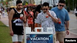 Hombres jóvenes leen las precauciones de seguridad pública mientras disfrutan de los bares y restaurantes en South Beach durante las vacaciones de primavera en medio de la pandemia del coronavirus, en Miami, el 27 de marzo de 2021.