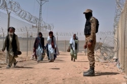 FILE - In this Aug. 20, 2021, file photo, Pakistani army soldier stands guard while Afghan people enter into Pakistan through a border crossing point, in Chaman, Pakistan. Chaman is a key border crossing between Pakistan and Afghanistan.