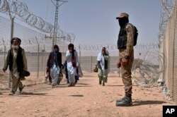 FILE - In this Aug. 20, 2021, file photo, Pakistani army soldier stands guard while Afghan people enter into Pakistan through a border crossing point, in Chaman, Pakistan. Chaman is a key border crossing between Pakistan and Afghanistan.