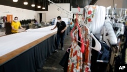 Workers at F.A.B.R.I.C., a non-profit organization, fold a large roll of fabric to make personal protective equipment after converting the fashion design warehouse to make gowns for area Dignity Health employees due to the coronavirus, April 13, 2020.