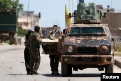 FILE - Kurdish fighters from the People's Protection Units (YPG) stand near a military vehilce in the southeast of Qamishli city, Syria, April 22, 2016.