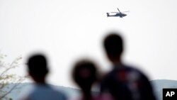 Migrants watch a helicopter of Greek army during exercises near the makeshift camp at the northern Greek border point of Idomeni, Greece, April 14, 2016.