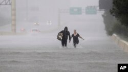 Two people walk down a flooded section of Interstate 610 in floodwaters from Tropical Storm Harvey, Aug. 27, 2017, in Houston, Texas. 
