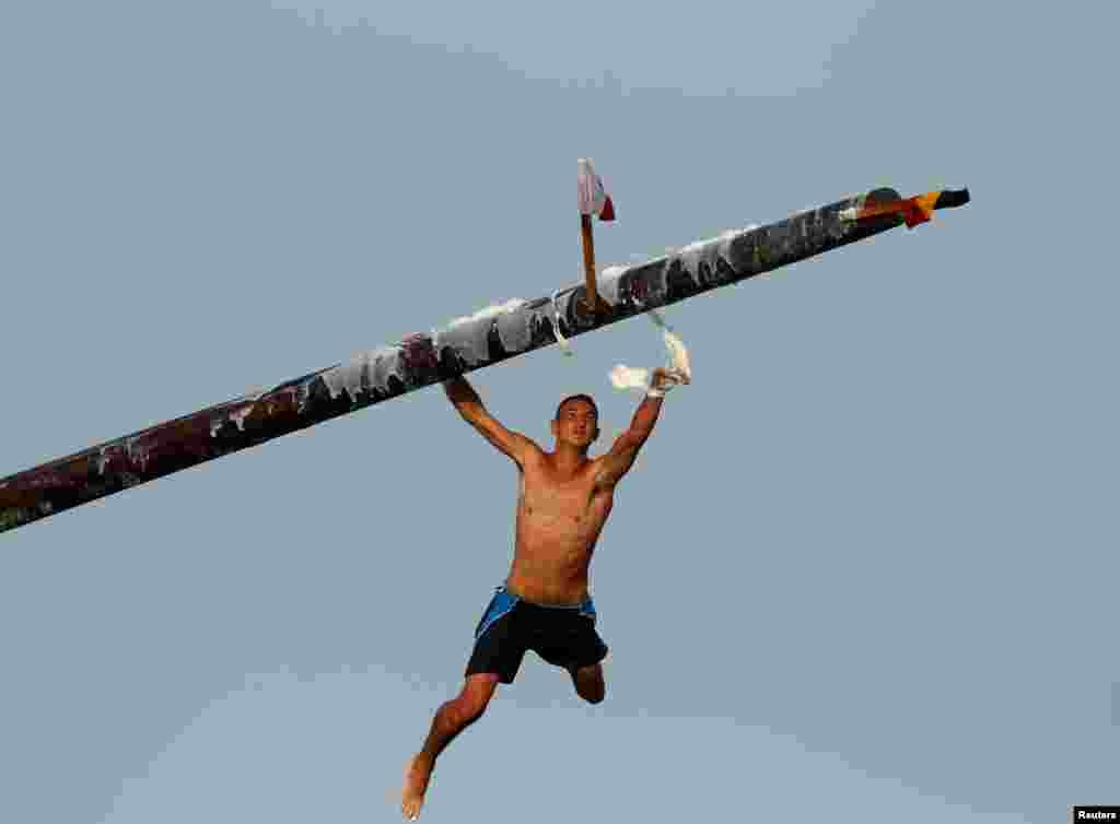 A competitor swipes lard off the &quot;gostra&quot;, a pole covered in lard, as he falls into the sea during the celebrations of the religious feast of St Julian, patron of the town of St Julian&#39;s, Malta.