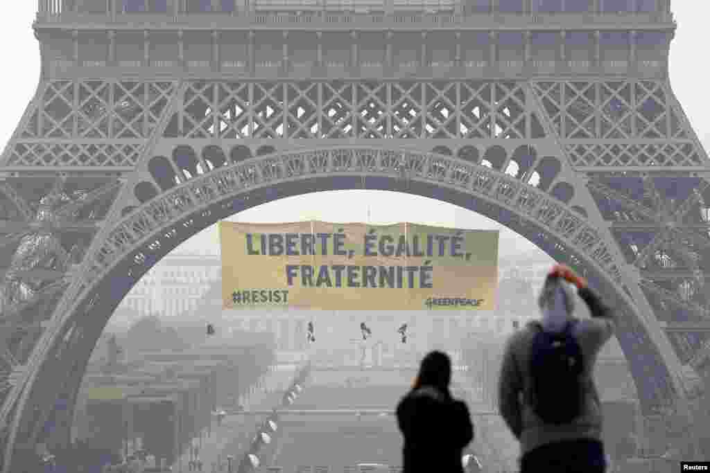 Para turis berjalan di alun-alun Trocadero saat para aktivis dari kelompok lingkungan Greenpeace membentangkan spanduk raksasa di Menara Eiffel yang bertuliskan &quot;Liberty, Equality, Fraternity&quot; dalam sebuah seruan pada warga negara Prancis untuk memberikan suara melawan calon presiden Front Nasional Marine Le Pen, di Paris.