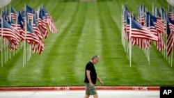 A man walks past a row of flags as he visits a park, Friday, May 15, 2020, in Kansas City, Missouri.