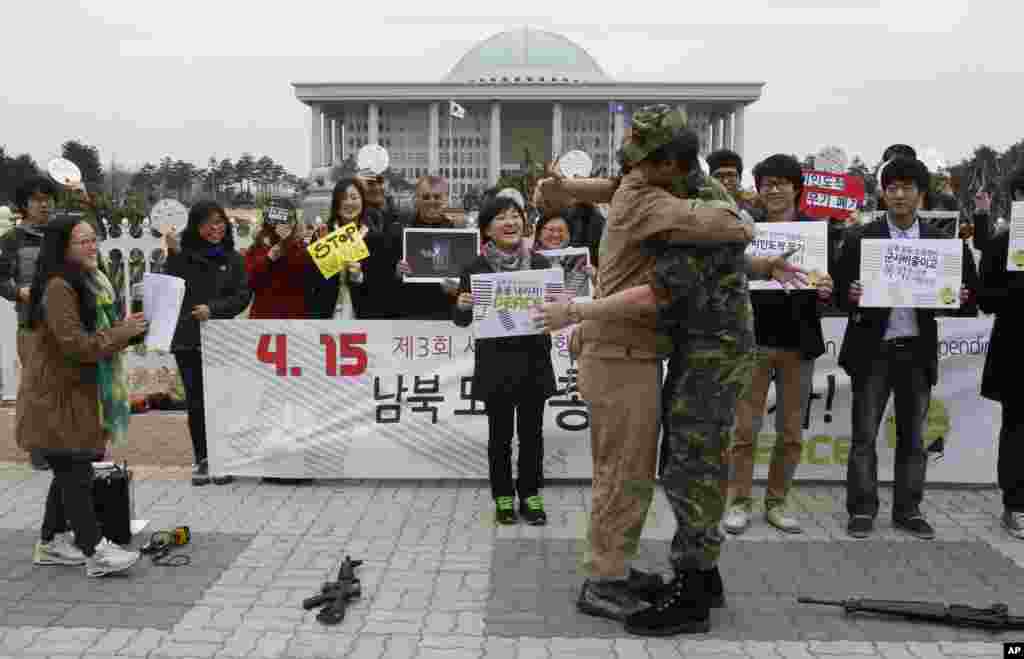 Anti-war activists wearing military clothes of a North, left, and South Korean hug each other during a rally to mark Global Day of Action on Military Spending in front of the National Assembly in Seoul, April 15, 2013.