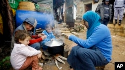 FILE - A Syrian refugee woman with her children prepares food near her tent in a camp for Syrians who fled their country’s civil war, in the Chouf mountain town of Ketermaya, Lebanon. 