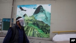 FILE - A man wearing a mask and a face shield to curb the spread of the new coronavirus walks near a mural depicting the ruins of Machu Picchu, in Lima, Peru, Sept. 10, 2020.