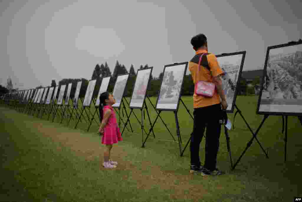 A South Korean girl listens to her grandfather as they stand before a photo exhibition of the Korean War at the National Cemetery in Seoul as the country marks the 64th anniversary of the start of the Korean War. 