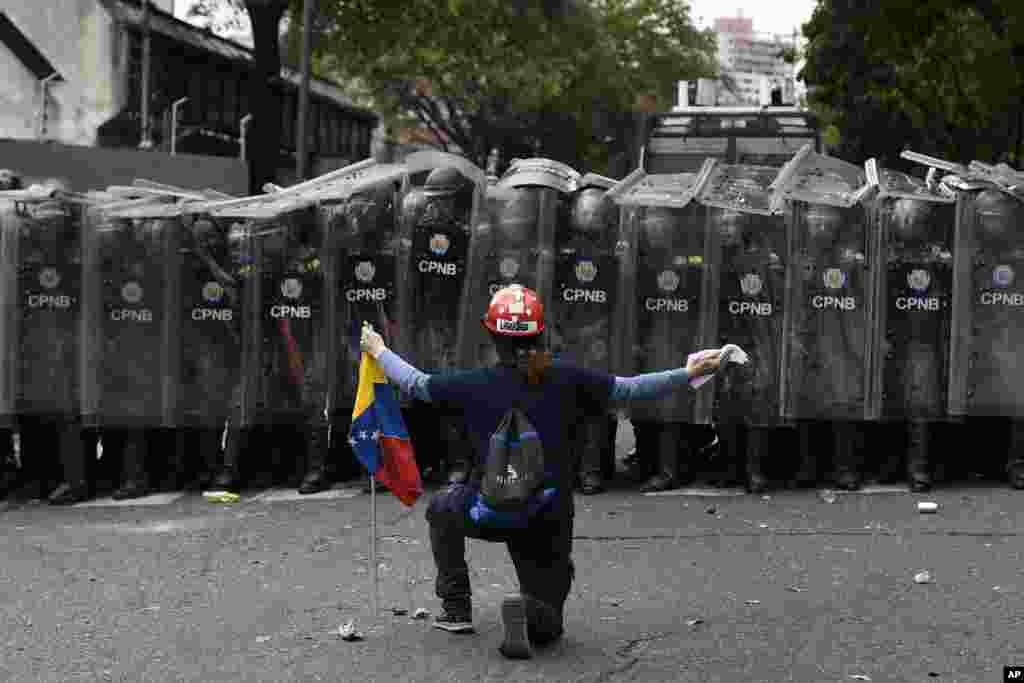 A man kneels in front of police blocking a march called by opposition political leader Juan Guaido in Caracas, Venezuela.