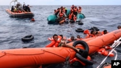 FILE - Migrants aboard a rubber boat end up in the water while others cling on to a centifloat before being rescued by a team of the Sea Watch-3, around 35 miles away from Libya, Oct. 18, 2021. 