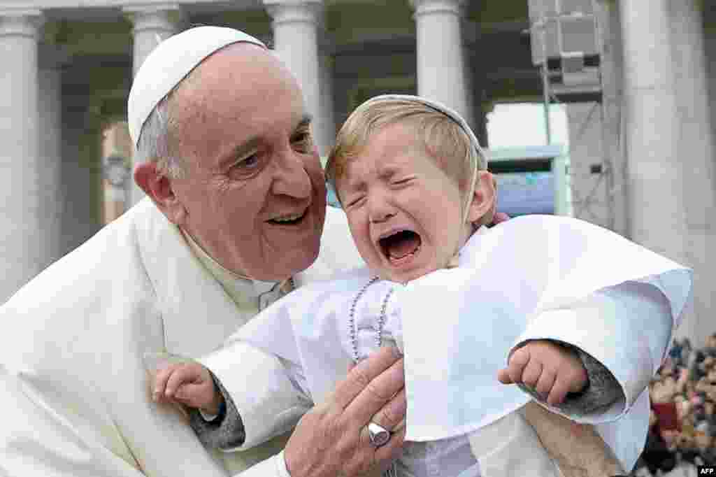 Paus Fransiskus mencium seorang anak laki-laki yang berpakaian seperti Paus ketika tiba untuk menemui khalayak umum di Lapangan St Petrus di Vatikan.