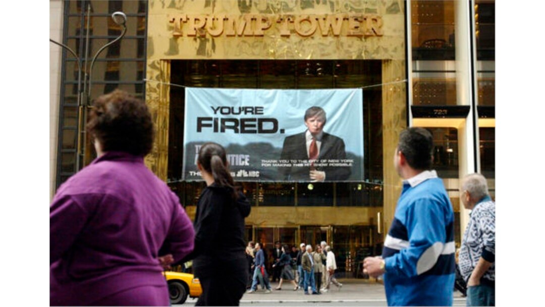 In this Saturday, March 27, 2004 file photo, passersby look at a sign advertising the reality television show, "The Apprentice," displayed at the entrance to the Trump Tower building in New York.