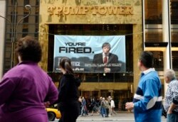 FILE - In this Saturday, March 27, 2004 file photo, passersby look at a sign advertising the reality television show, "The Apprentice," displayed at the entrance to the Trump Tower building in New York.