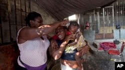 Residents douse a little girl's face with water after tear gas was fired by National Police near their home during clashes with anti-government protesters in Port-au-Prince, Haiti, Dec. 13, 2014.